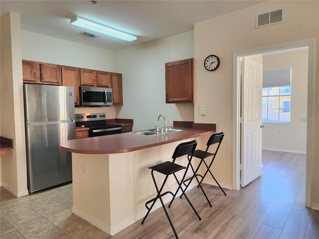 A kitchen with wood cabinets, stainless steel appliances, and a breakfast bar with two chairs — 8137 CLAIRE ANN DRIVE UNIT 203, ORLANDO, FL