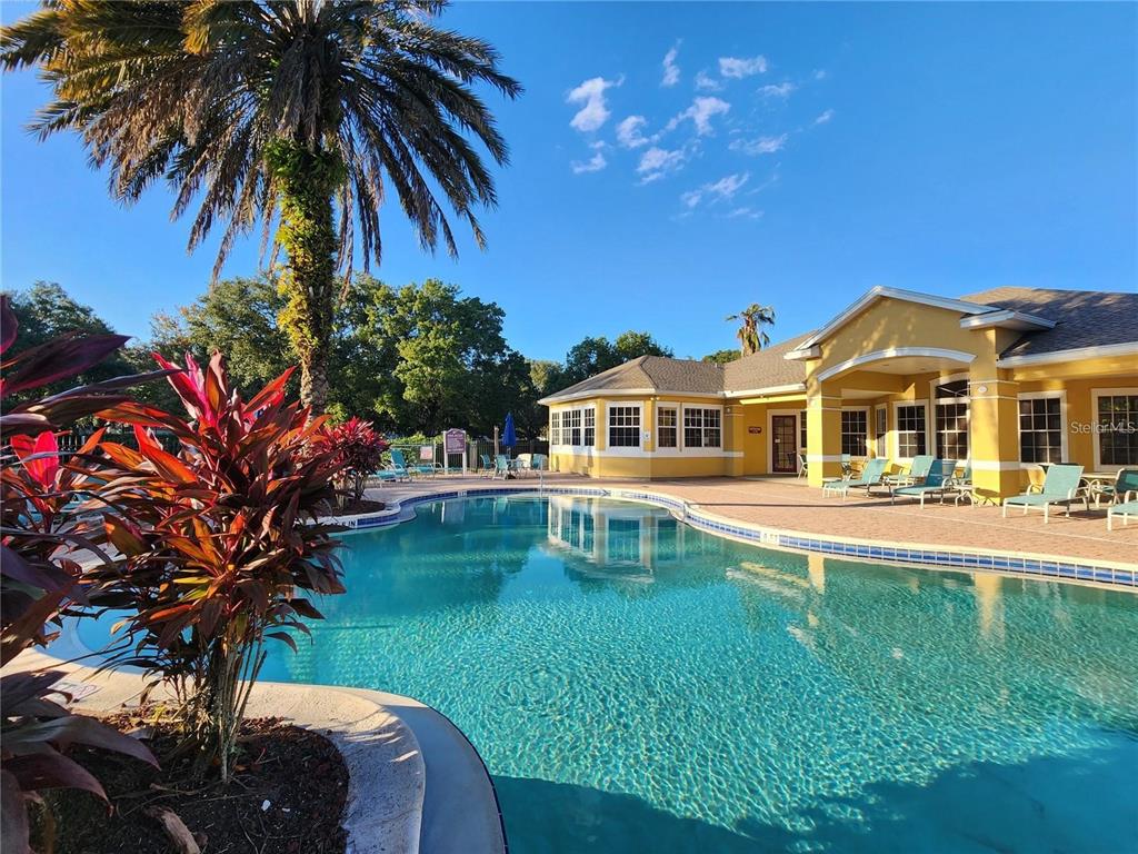 A swimming pool sits in front of a yellow clubhouse with a palm tree nearby — 8137 CLAIRE ANN DRIVE UNIT 203, ORLANDO, FL