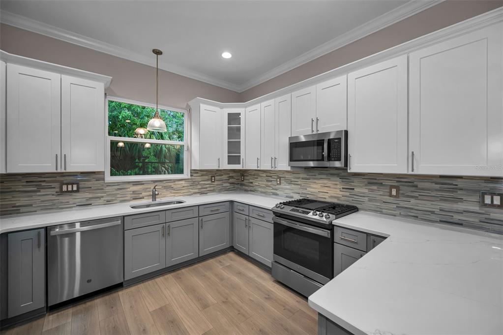 A kitchen features white upper cabinets, gray lower cabinets, stainless steel appliances, and a tiled backsplash — 726 GRAND CYPRESS LANE, TARPON SPRINGS, FL