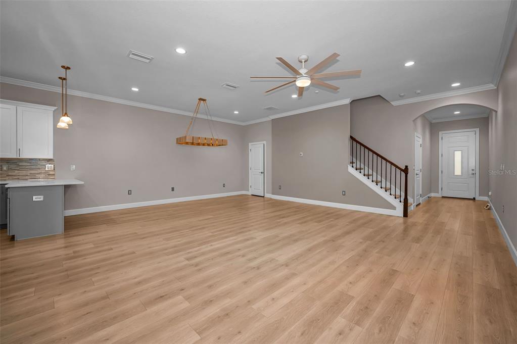 An open-concept living and dining area features light wood flooring, white furniture, and a staircase — 726 GRAND CYPRESS LANE, TARPON SPRINGS, FL