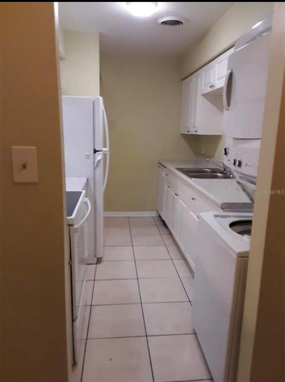 A narrow galley kitchen features white cabinets, white appliances, and light-colored floor tiles — 501 E BAY DRIVE UNIT 1104, LARGO, FL