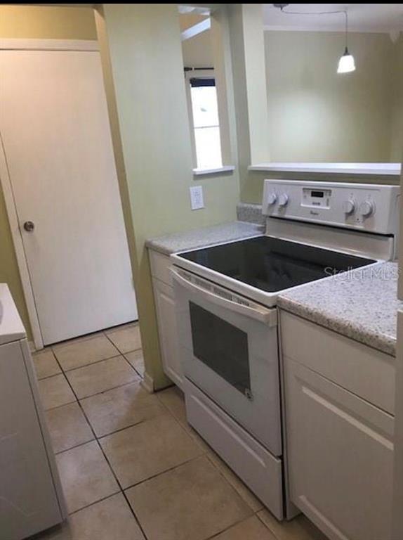 A kitchen features a white electric range, light-colored cabinets, speckled countertops, and tile flooring — 501 E BAY DRIVE UNIT 1104, LARGO, FL