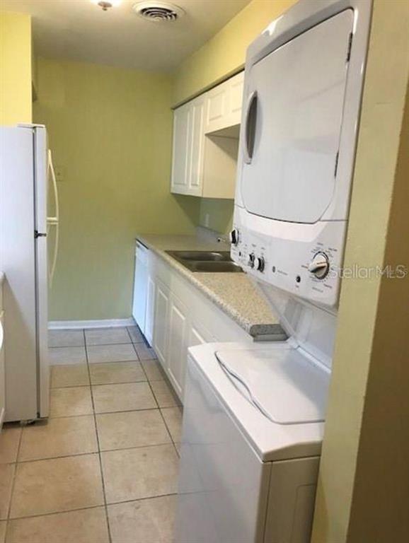 A kitchen features white cabinets, a refrigerator, a stacked washer-dryer unit, and tiled flooring — 501 E BAY DRIVE UNIT 1104, LARGO, FL