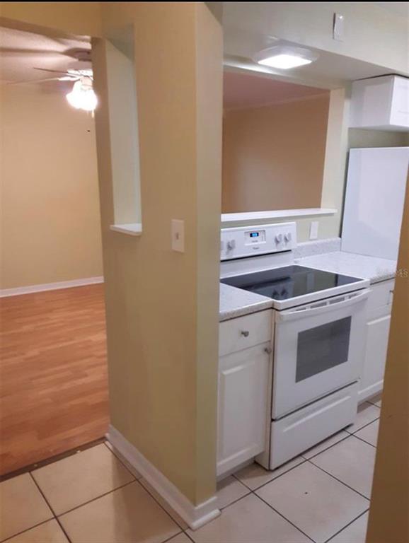A kitchen with white appliances and cabinets overlooks a living area with wood-look flooring — 501 E BAY DRIVE UNIT 1104, LARGO, FL