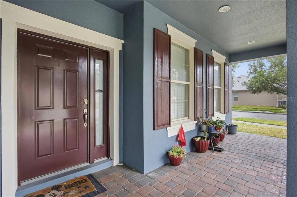 A front porch with a dark brown door, blue siding, and potted plants on pavers — 8721 BAYVIEW CROSSING DRIVE, WINTER GARDEN, FL