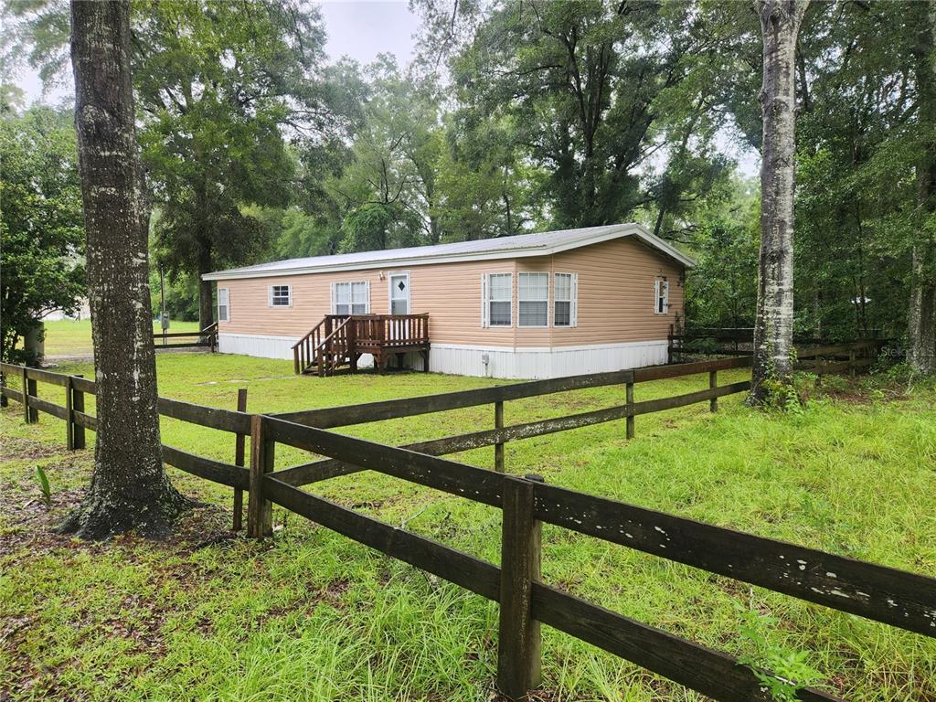 A tan mobile home sits on a grassy lot enclosed by a wooden post-and-rail fence — 1182 NW 27TH TERRACE, BELL, FL