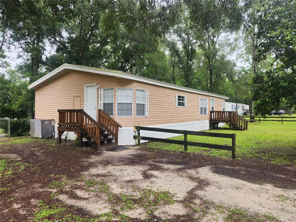 A tan mobile home with wooden stairs and a black fence sits on a grassy lot — 1182 NW 27TH TERRACE, BELL, FL