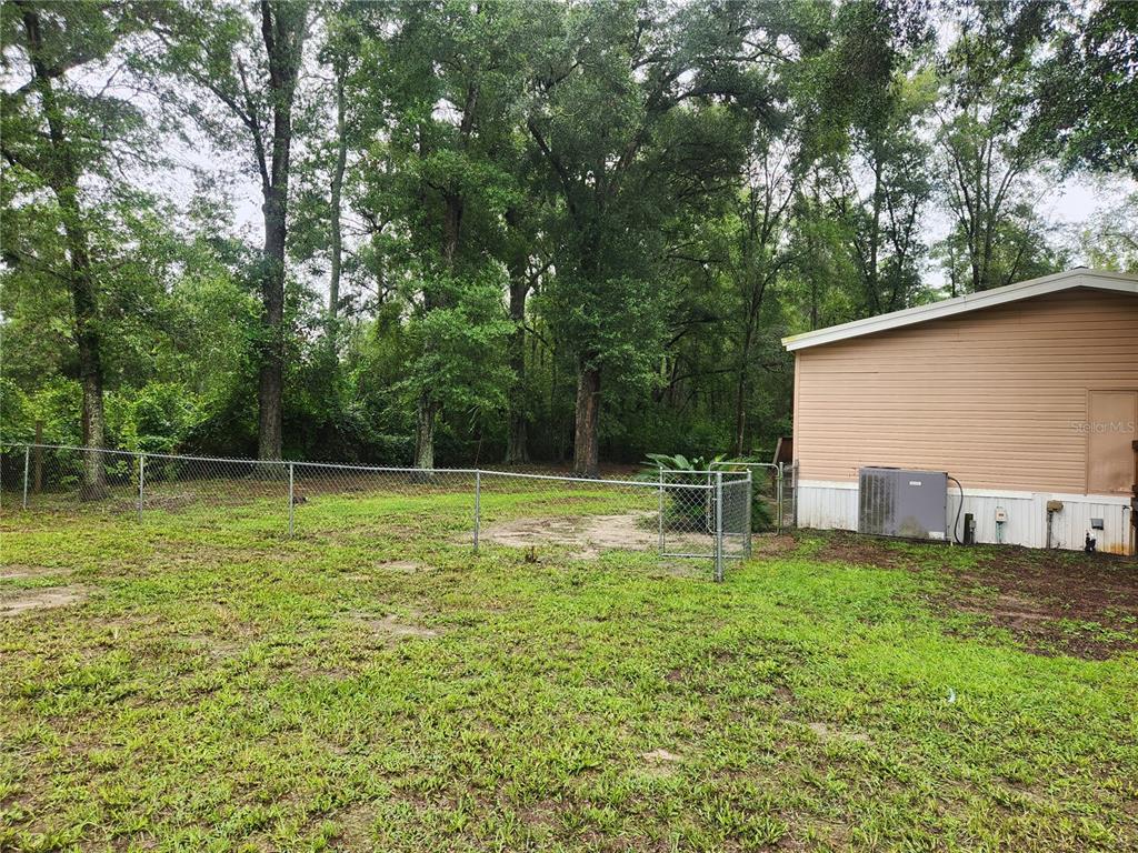 A chain-link fence encloses a grassy backyard next to the side of a tan house — 1182 NW 27TH TERRACE, BELL, FL