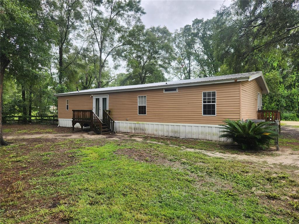 A tan mobile home with a metal roof and wooden deck sits on a grassy lot — 1182 NW 27TH TERRACE, BELL, FL