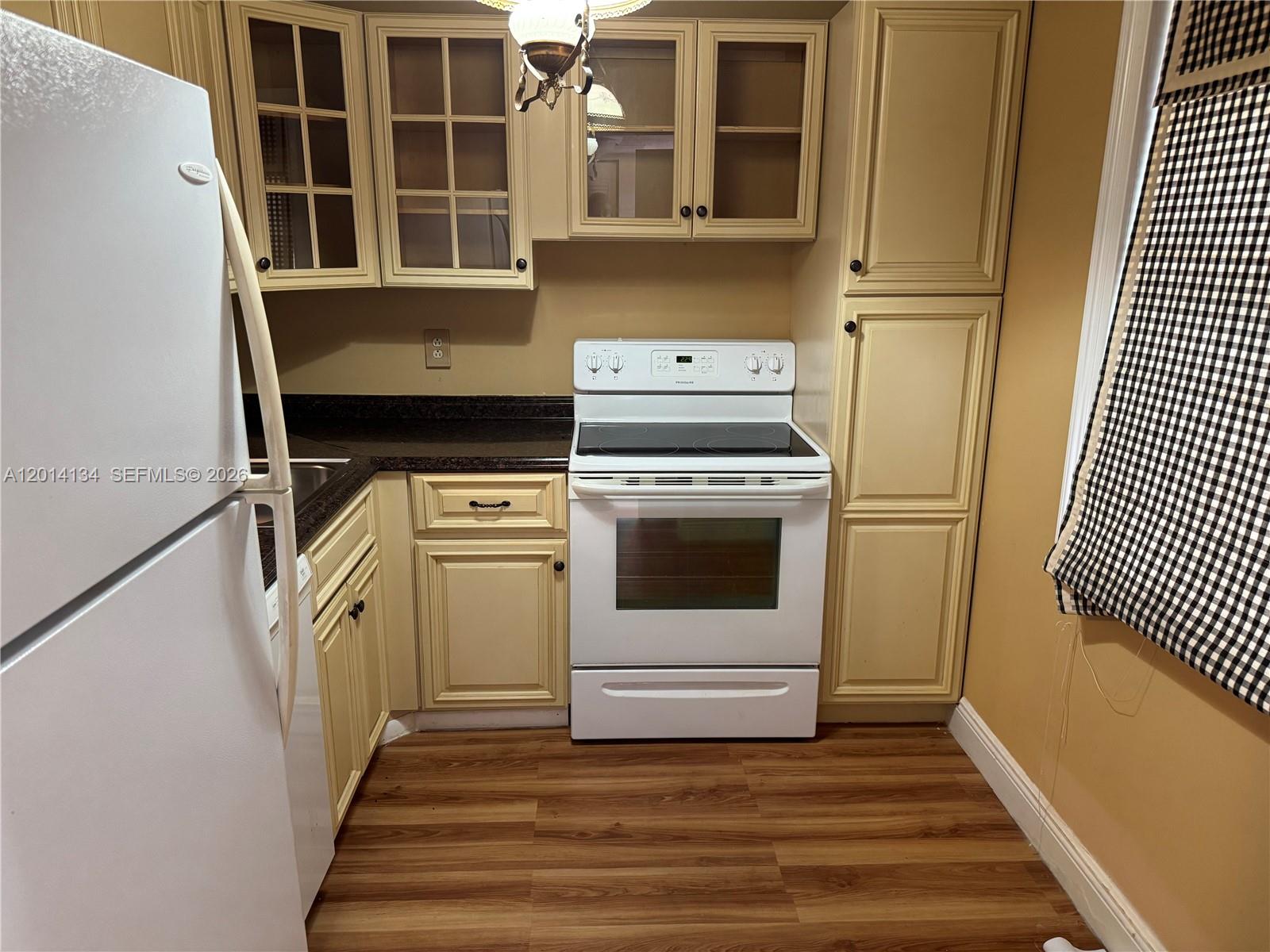 A kitchen features cream-colored cabinets, a white stove, a white refrigerator, and wood-look flooring — 3774 Inverrary Blvd # 106P, Lauderhill FL 33319, LAUDERHILL, FL