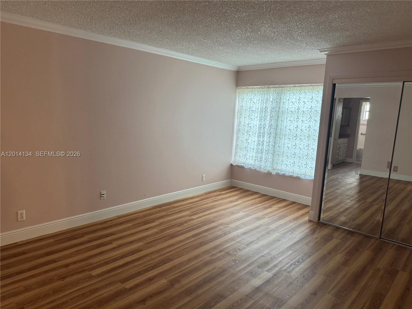 A bedroom features light pink walls, wood-look flooring, a large window, and mirrored closet doors — 3774 Inverrary Blvd # 106P, Lauderhill FL 33319, LAUDERHILL, FL