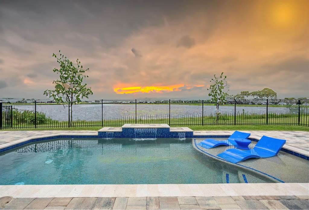 A swimming pool with a sun shelf and water feature overlooks a lake at sunset — 18405 MOWRY COURT, ORLANDO, FL