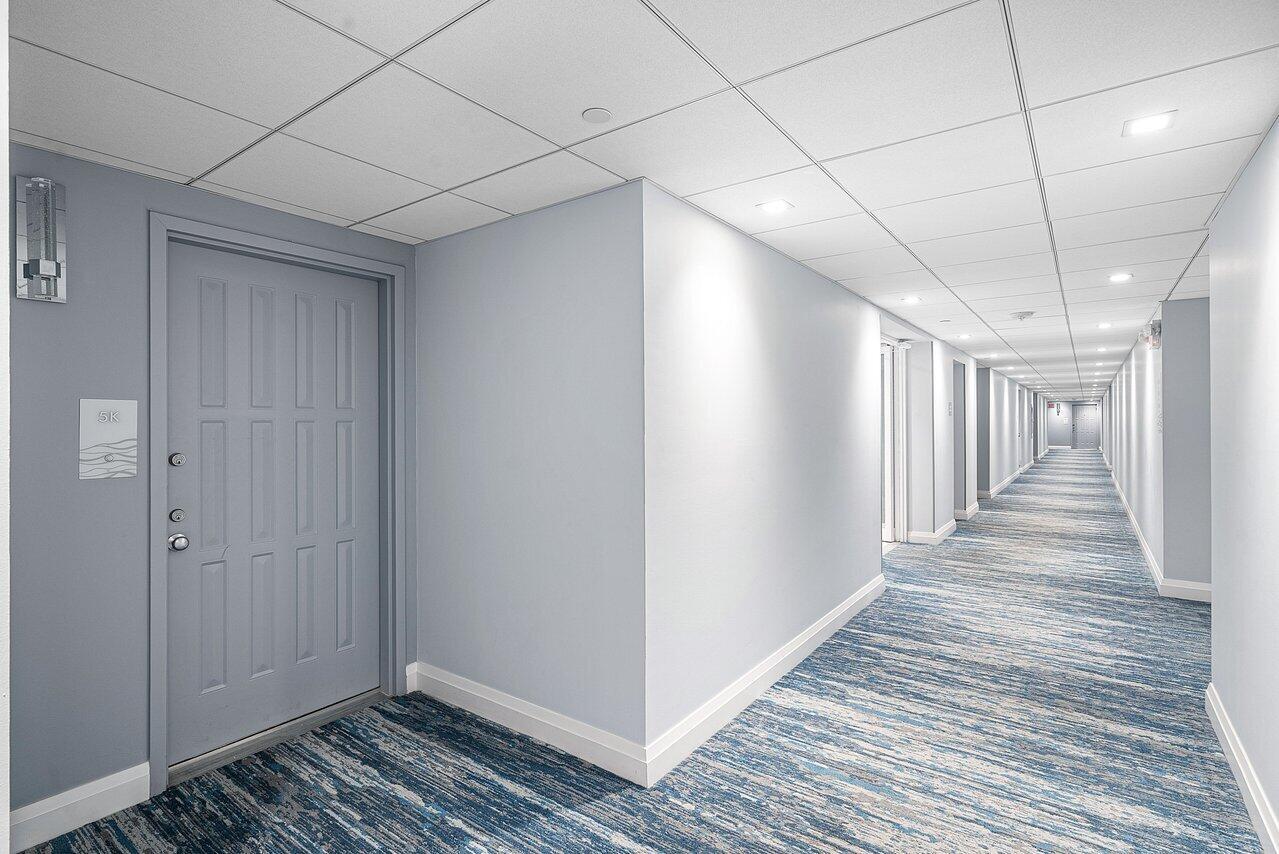 A long hotel hallway features light blue walls, a patterned blue carpet, and recessed lighting — 3400 S Ocean Boulevard # 5k, Highland Beach FL 33487, HIGHLAND BEACH, FL