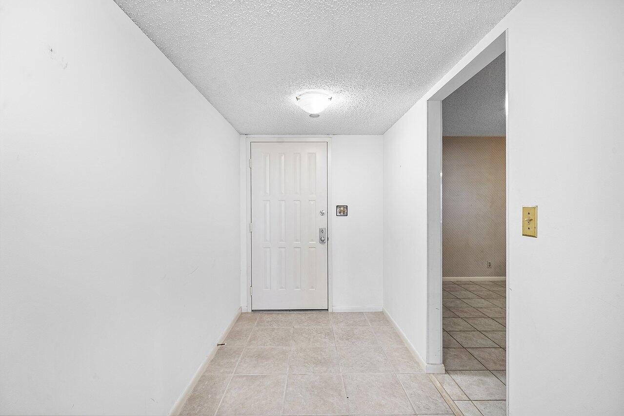 A white front door opens into a small entryway with tiled flooring and white walls — 3400 S Ocean Boulevard # 5k, Highland Beach FL 33487, HIGHLAND BEACH, FL