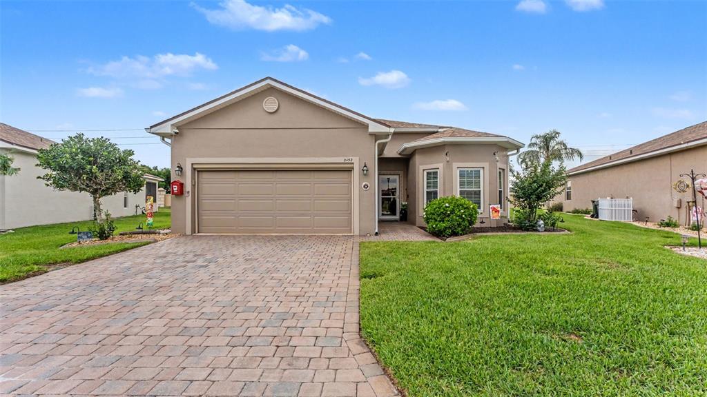 A single-story house with a beige stucco exterior, a paved driveway, and a two-car garage — 2452 SALZBURG LOOP, WINTER HAVEN, FL