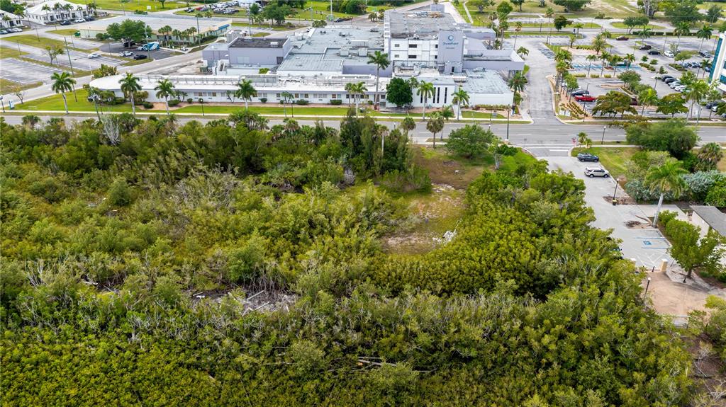 An aerial view shows a vacant, tree-covered lot adjacent to a large commercial building and parking — 806 E MARION AVENUE, PUNTA GORDA, FL