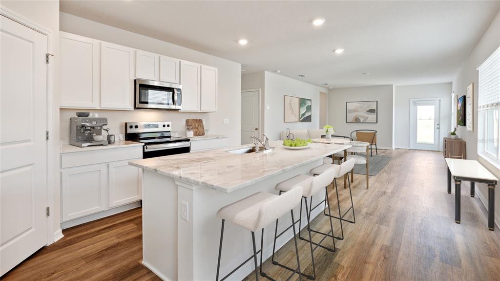A kitchen with white cabinets, a marble-topped island, and bar seating opens to a living area — 8828 CLEAR VIEW STREET, PARRISH, FL