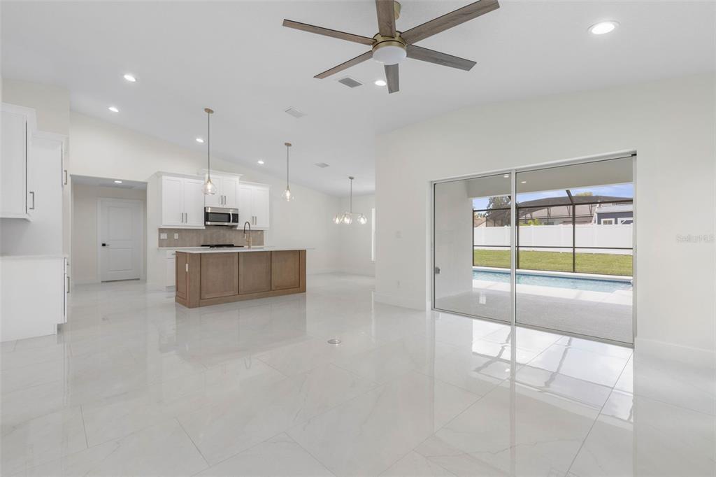 A bright, open-concept kitchen and living area with white tile floors, an island, and pool view — 32 FEDERAL LANE, PALM COAST, FL