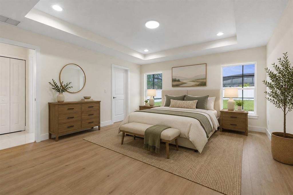 A bedroom features a tray ceiling, light wood flooring, a bed with neutral bedding, and furniture — 32 FEDERAL LANE, PALM COAST, FL