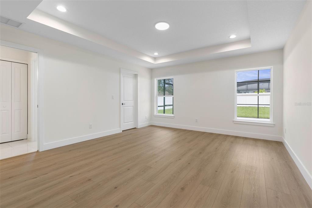 A bright bedroom features light wood-look flooring, white walls, a tray ceiling, and two windows — 32 FEDERAL LANE, PALM COAST, FL