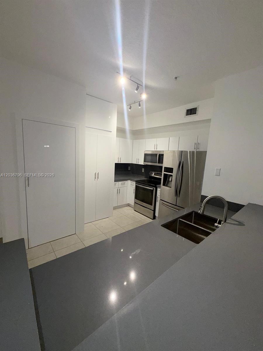 A modern kitchen features white cabinetry, stainless steel appliances, and a gray quartz countertop — 7220 NW 114th Ave # 20916, Doral FL 33178, DORAL, FL