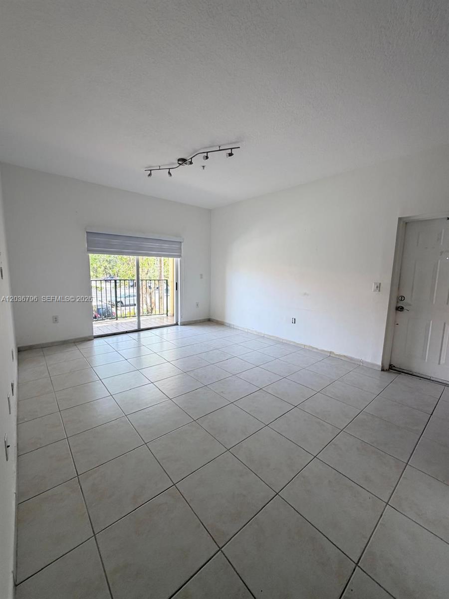 An empty living room features white walls, tile flooring, a sliding glass door, and track lighting — 7220 NW 114th Ave # 20916, Doral FL 33178, DORAL, FL