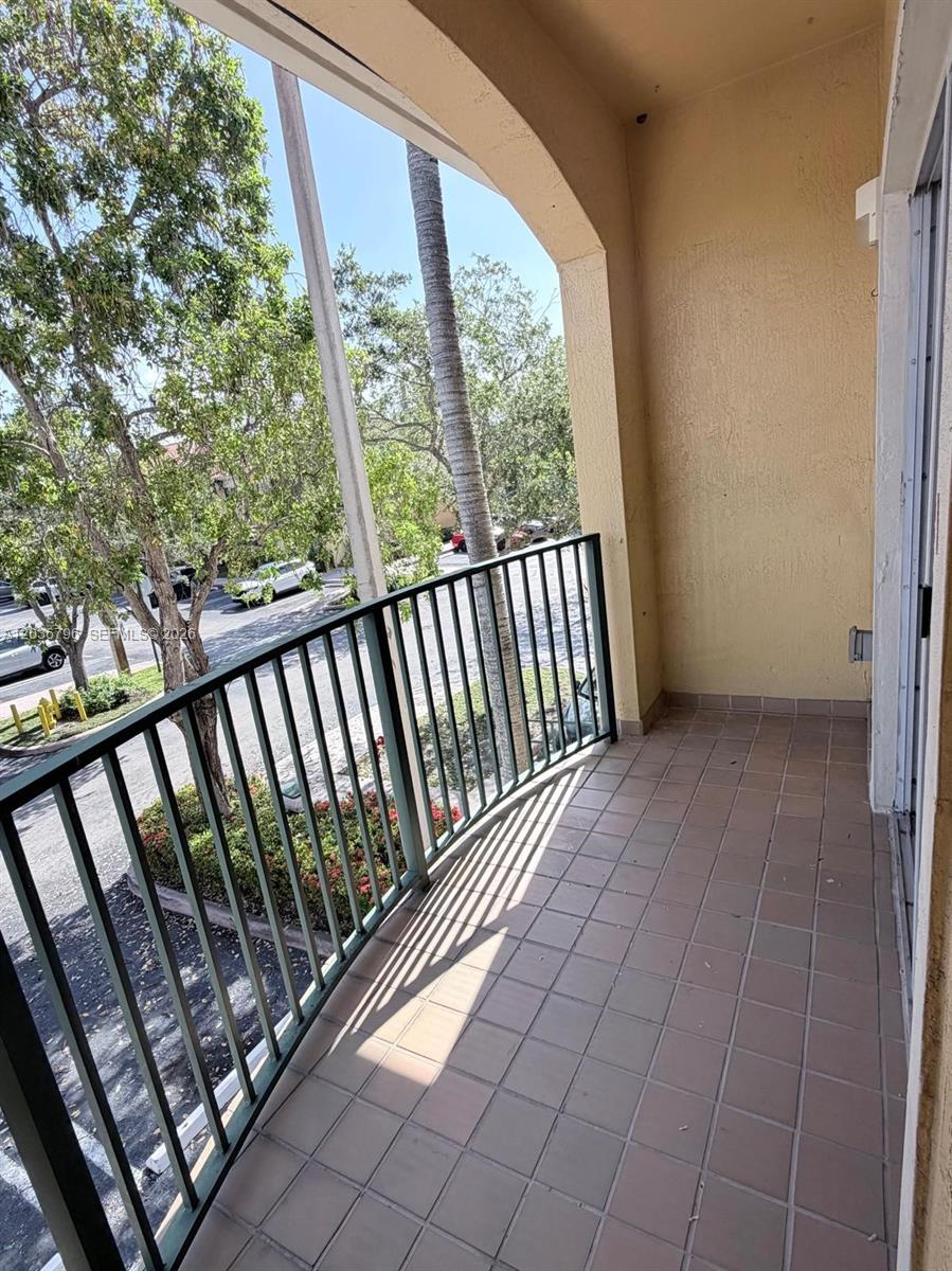A covered balcony features tiled flooring, a dark metal railing, and views of trees — 7220 NW 114th Ave # 20916, Doral FL 33178, DORAL, FL