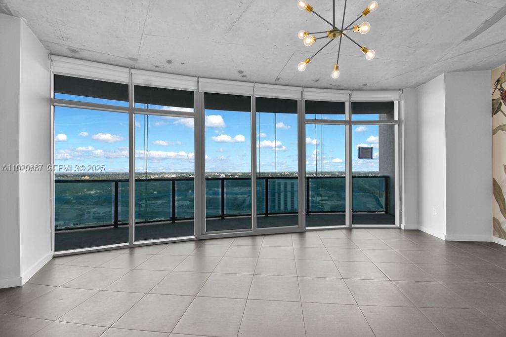 An empty room features large floor-to-ceiling windows, gray tile flooring, and a modern chandelier — 3301 NE 1st Ave # H2509, Miami FL 33137, MIAMI, FL