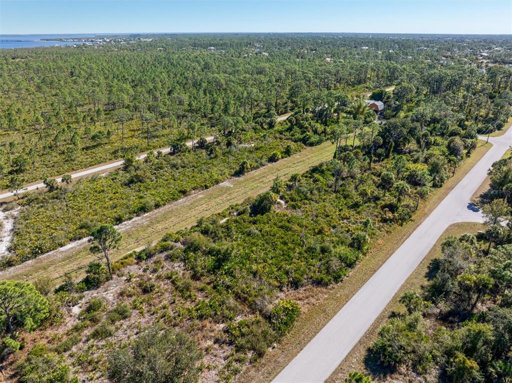 An aerial view shows a vacant, wooded lot bordered by a paved road and trees — 4388 SCHNEIDER STREET, PORT CHARLOTTE, FL