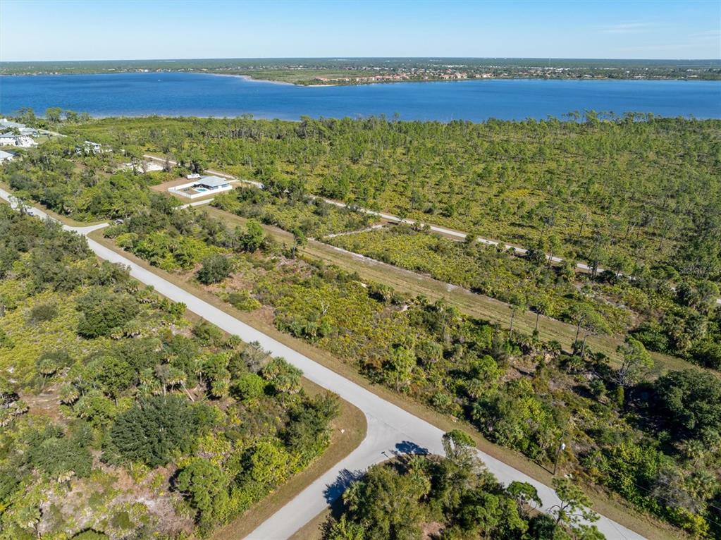 An aerial view shows a paved road winding through a wooded lot near a large body of water — 4388 SCHNEIDER STREET, PORT CHARLOTTE, FL
