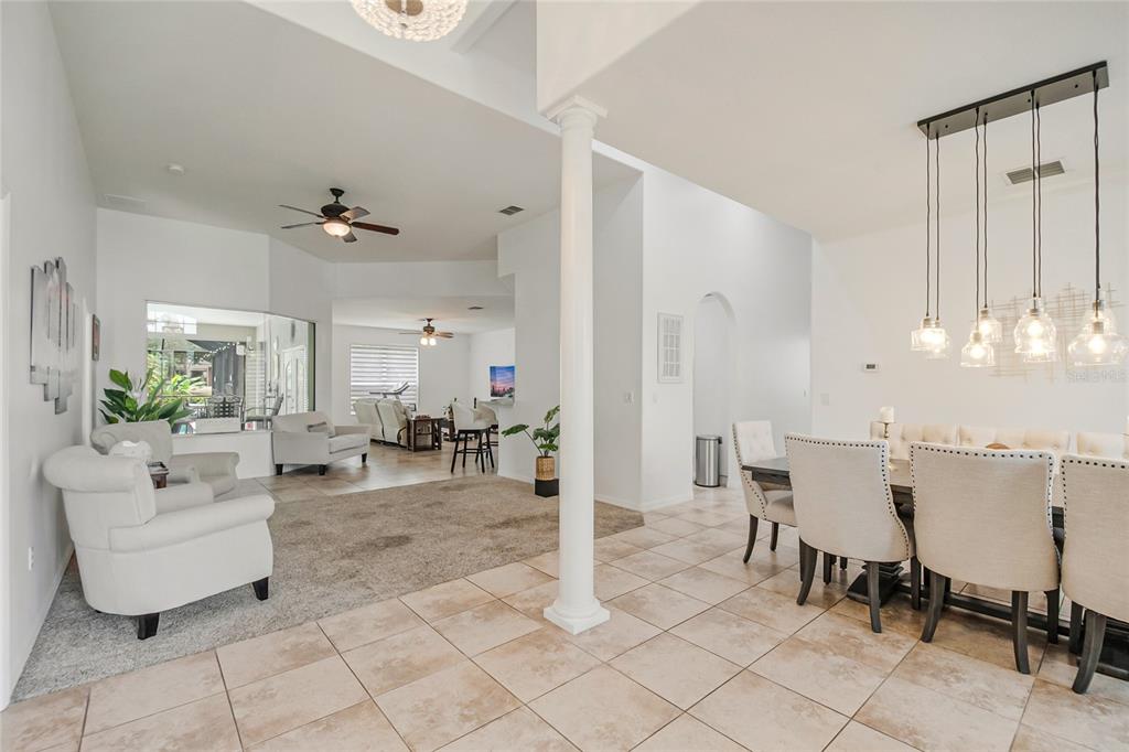 A bright open-concept living and dining area features tile flooring, a white pillar, and chandeliers — 2807 DEERFIELD STREET, ST CLOUD, FL