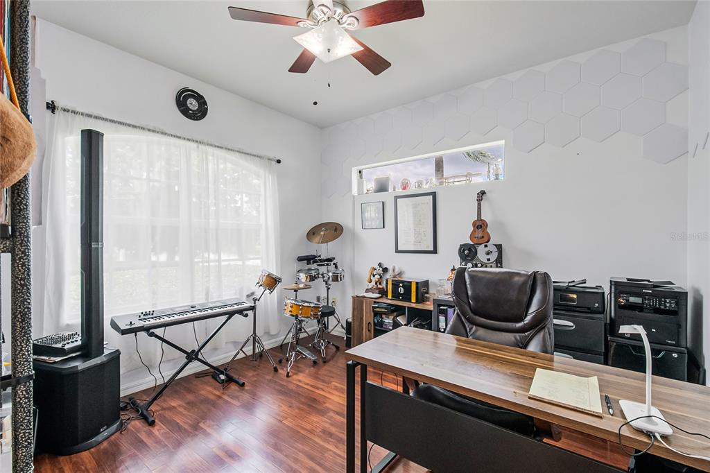 A home office features a desk, musical instruments, a ceiling fan, and white hexagonal wall panels — 2807 DEERFIELD STREET, ST CLOUD, FL