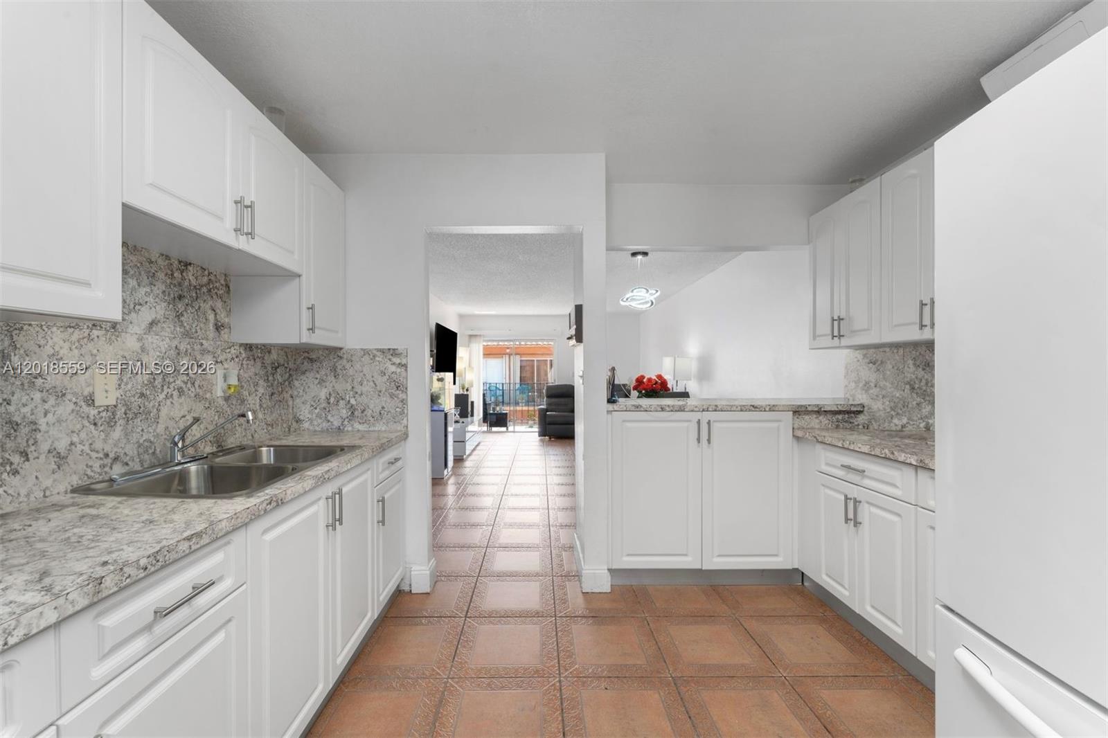 A kitchen features white cabinets, granite countertops, and tile flooring, opening to a living area — 1950 W 54th St # 406, Hialeah FL 33012, HIALEAH, FL