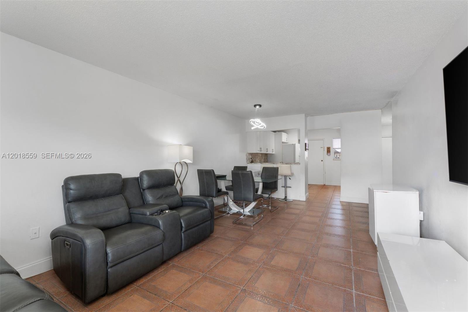A living and dining area features a grey leather sofa, tile flooring, and white walls — 1950 W 54th St # 406, Hialeah FL 33012, HIALEAH, FL