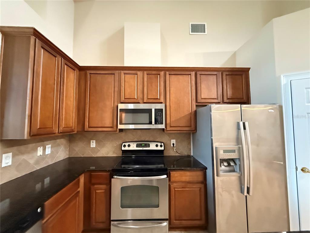 A kitchen features wood cabinets, stainless steel appliances, and dark countertops against a tiled backsplash — 10856 BREAKING ROCKS DRIVE, TAMPA, FL