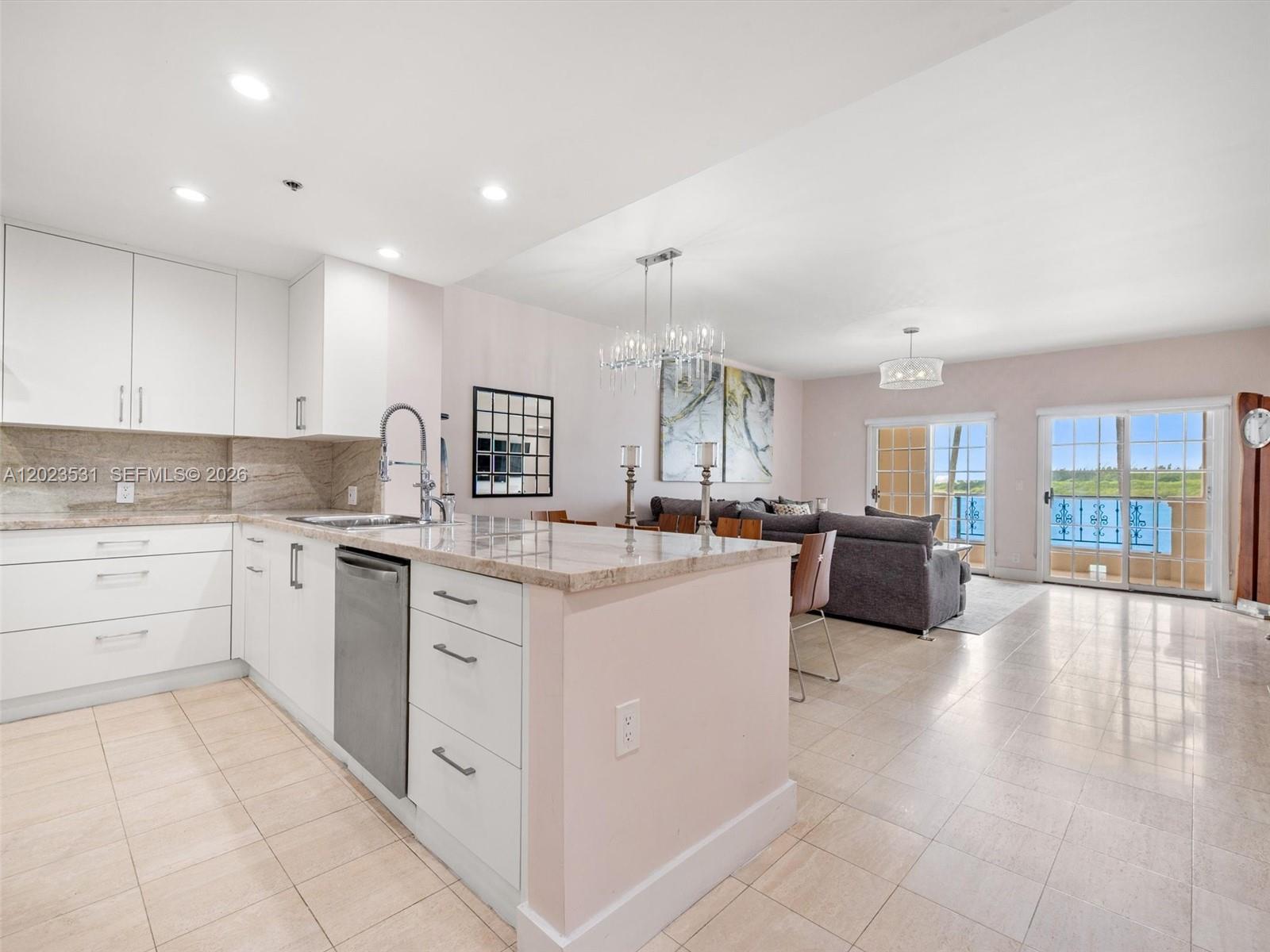 A modern kitchen with white cabinets and stone countertops opens into a living area — 2425 Fisher Island Dr # 5205, Miami Beach FL 33109, MIAMI BEACH, FL