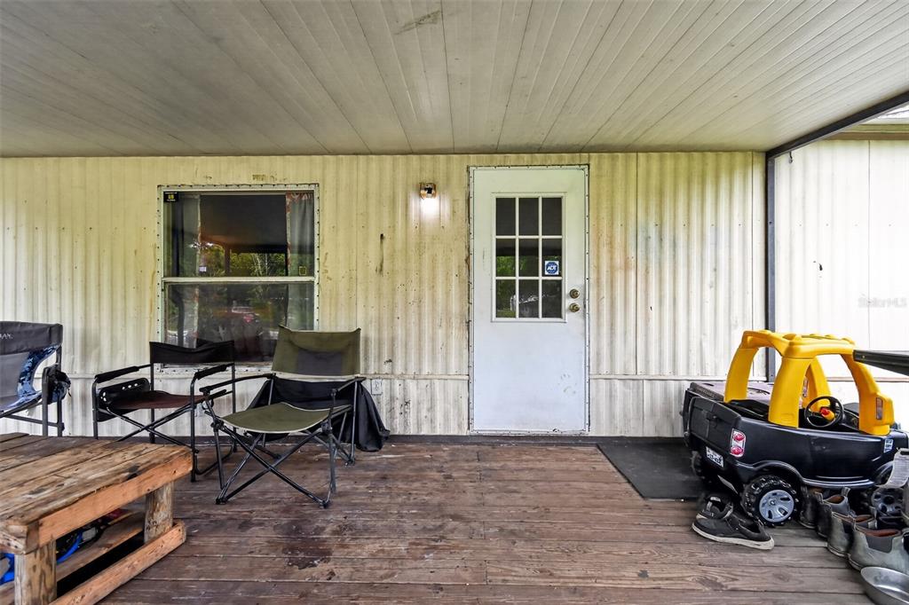 A covered wooden porch features a white door, a window, folding chairs, and a toy car — 25005 BARTHOLOMEW STREET, CHRISTMAS, FL
