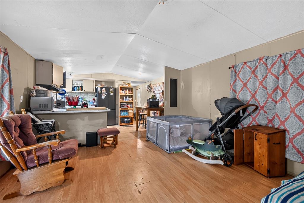 A living area with wood-look flooring, a rocking chair, a playpen, and an open kitchen — 25005 BARTHOLOMEW STREET, CHRISTMAS, FL