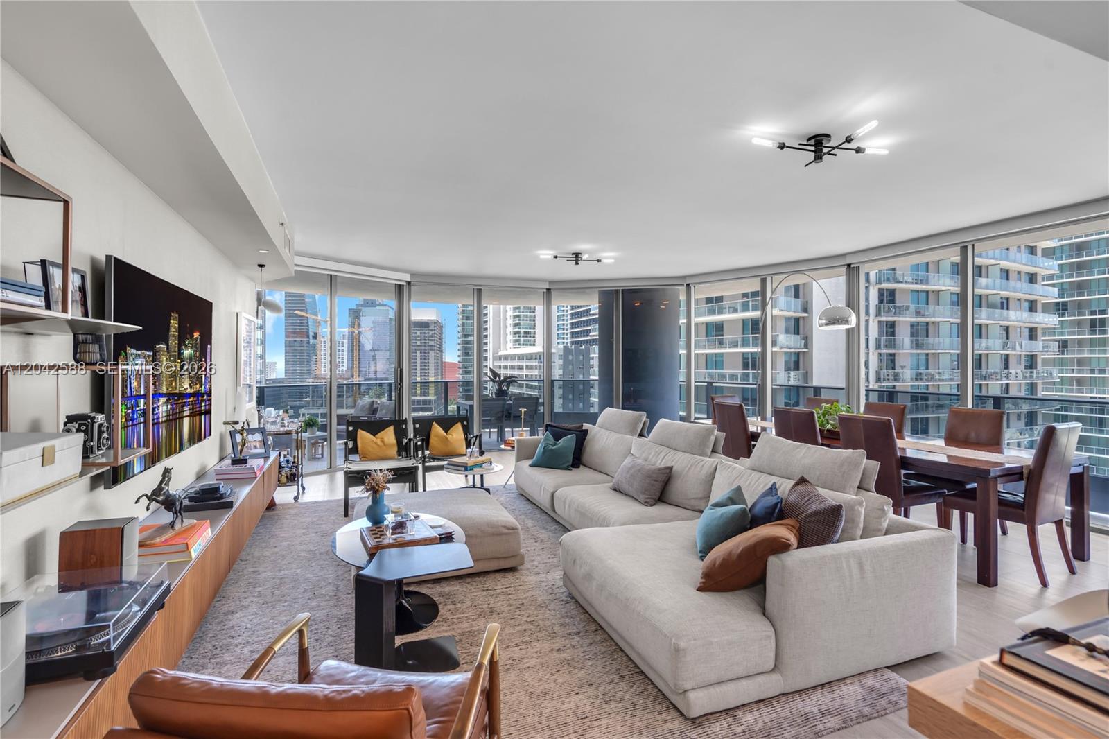 A modern living room features a large sectional sofa, dining area, and floor-to-ceiling city windows — 1000 Brickell Plz # 2402, Miami FL 33131, MIAMI, FL
