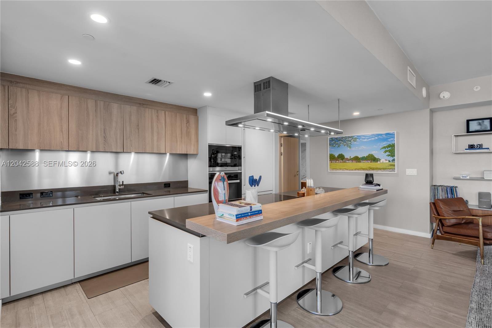 A modern kitchen features white lower cabinets, wood-toned upper cabinets, and a central island with seating — 1000 Brickell Plz # 2402, Miami FL 33131, MIAMI, FL