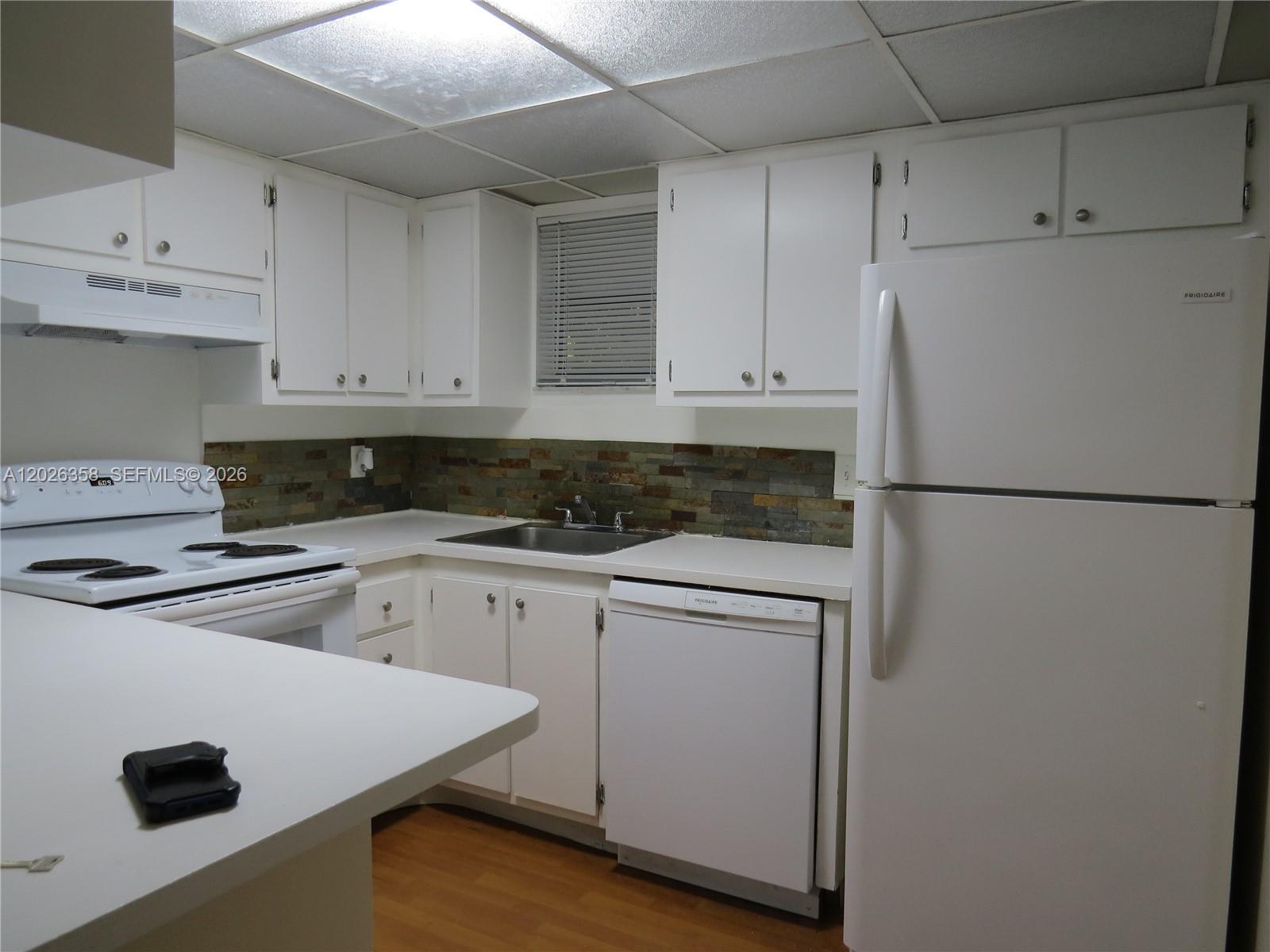 A kitchen features white cabinetry, white appliances, a stone backsplash, and a drop ceiling — 8290 Lake Dr # 143, Doral FL 33166, DORAL, FL