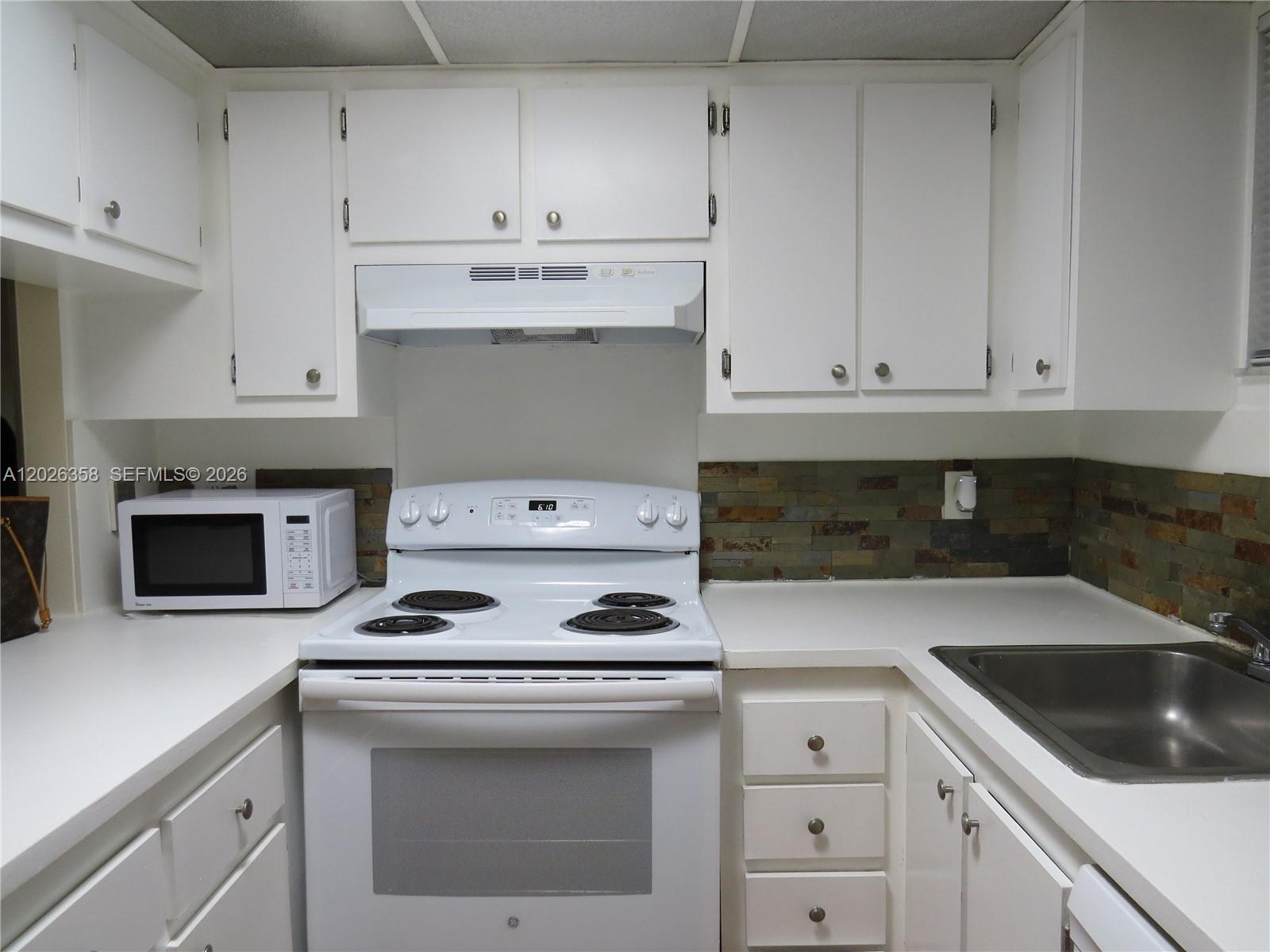 A kitchen features white cabinets, a white electric stove, a microwave, and a stone backsplash — 8290 Lake Dr # 143, Doral FL 33166, DORAL, FL