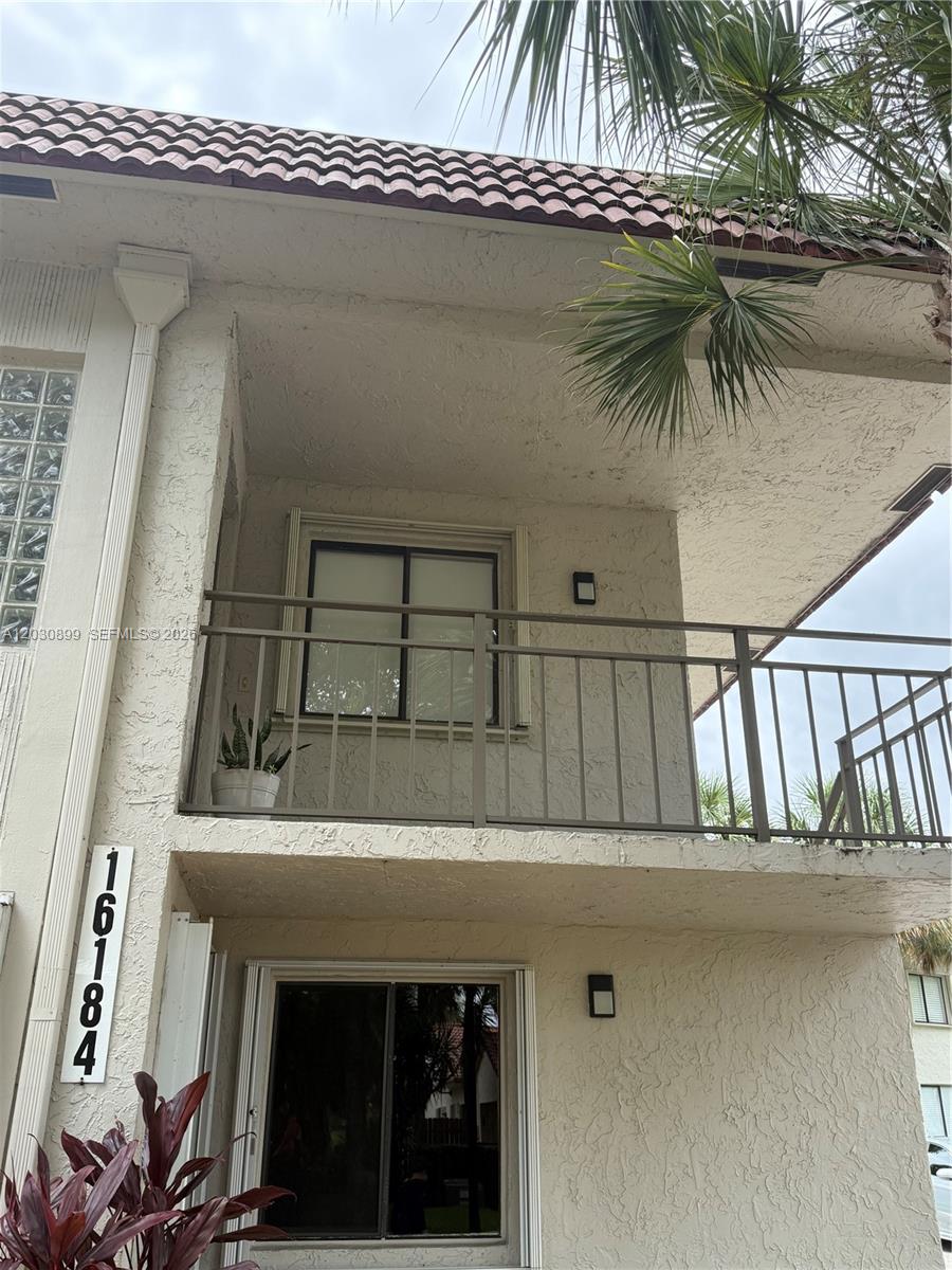 A two-story exterior view shows a balcony with metal railings and a glass sliding door — 16184 Laurel Dr # 204, Weston FL 33326, WESTON, FL