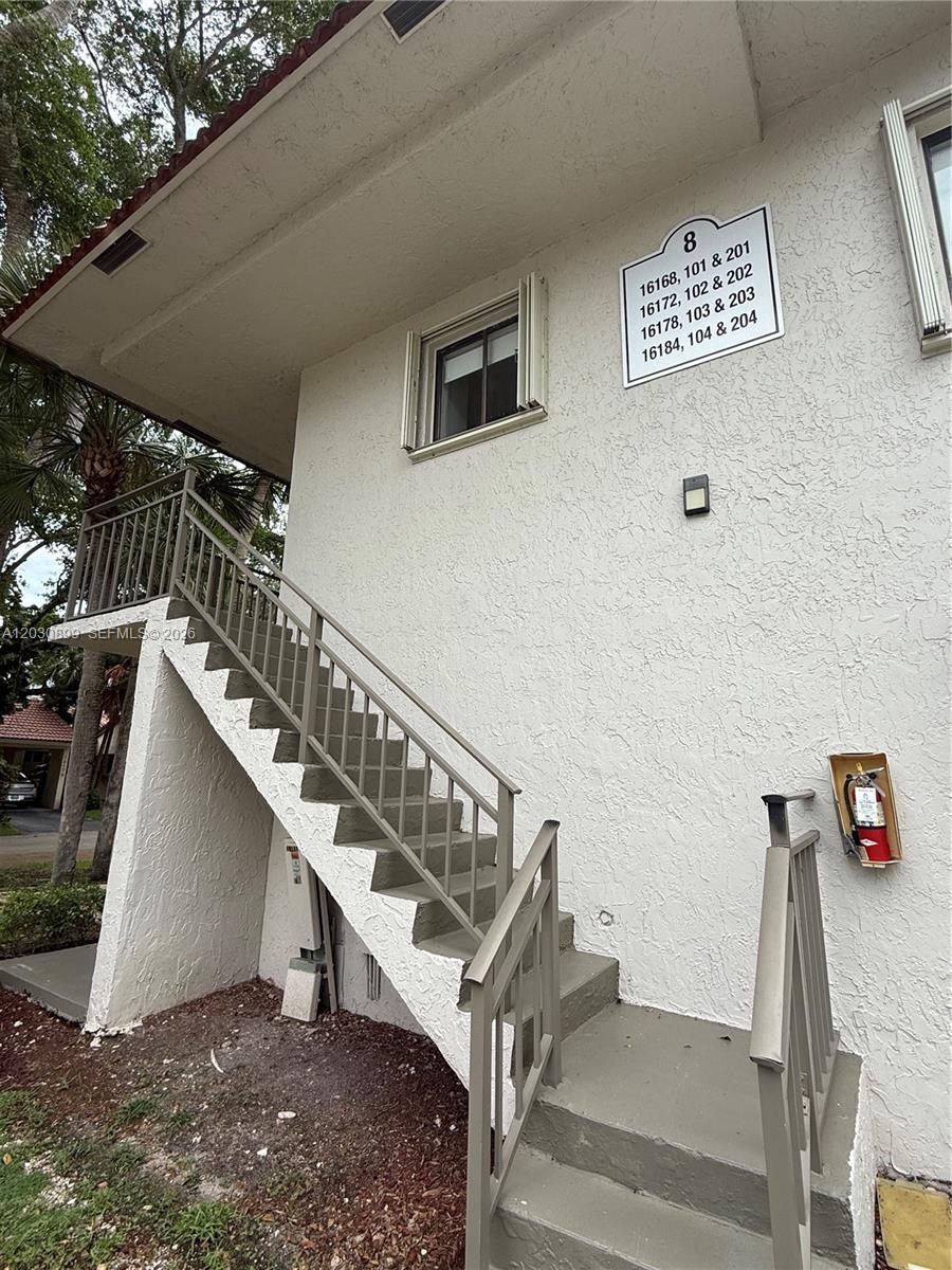 An exterior view of a two-story apartment building with a concrete staircase and fire extinguisher — 16184 Laurel Dr # 204, Weston FL 33326, WESTON, FL