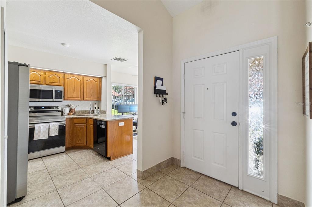 An entryway with tiled floors leads into a kitchen featuring wooden cabinets and stainless appliances — 3344 GRAY FOX COVE UNIT 4, APOPKA, FL