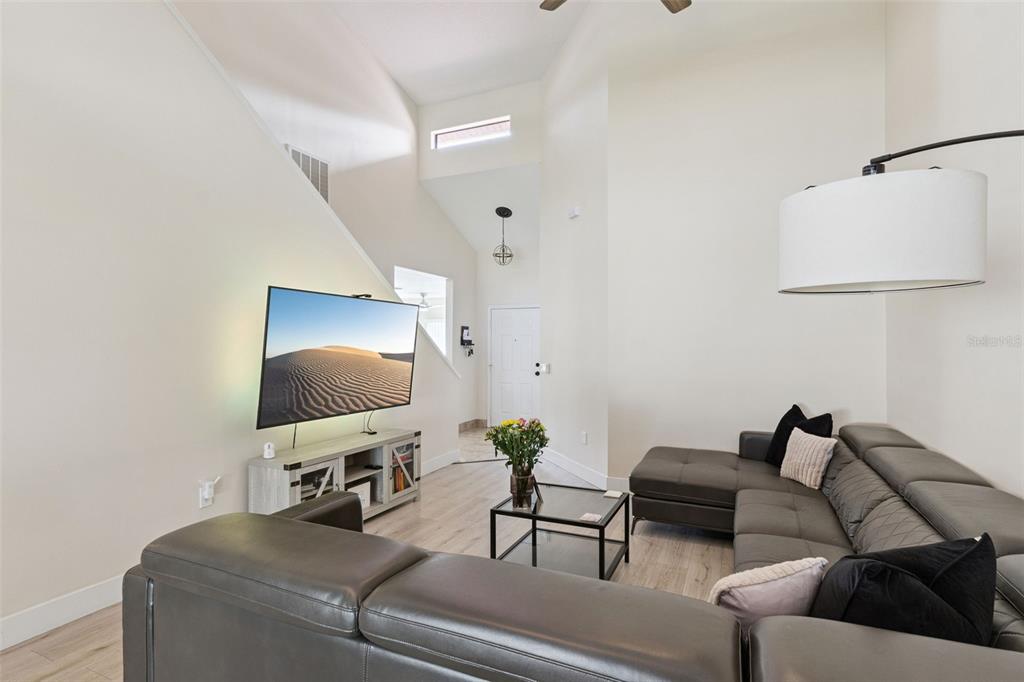 A living room features a grey sectional sofa, a wall-mounted television, and light wood flooring — 3344 GRAY FOX COVE UNIT 4, APOPKA, FL