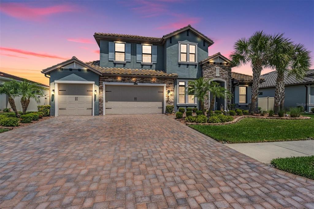 A two-story house with a stone facade, blue siding, and a paved driveway at sunset — 29043 PICANA LANE, WESLEY CHAPEL, FL