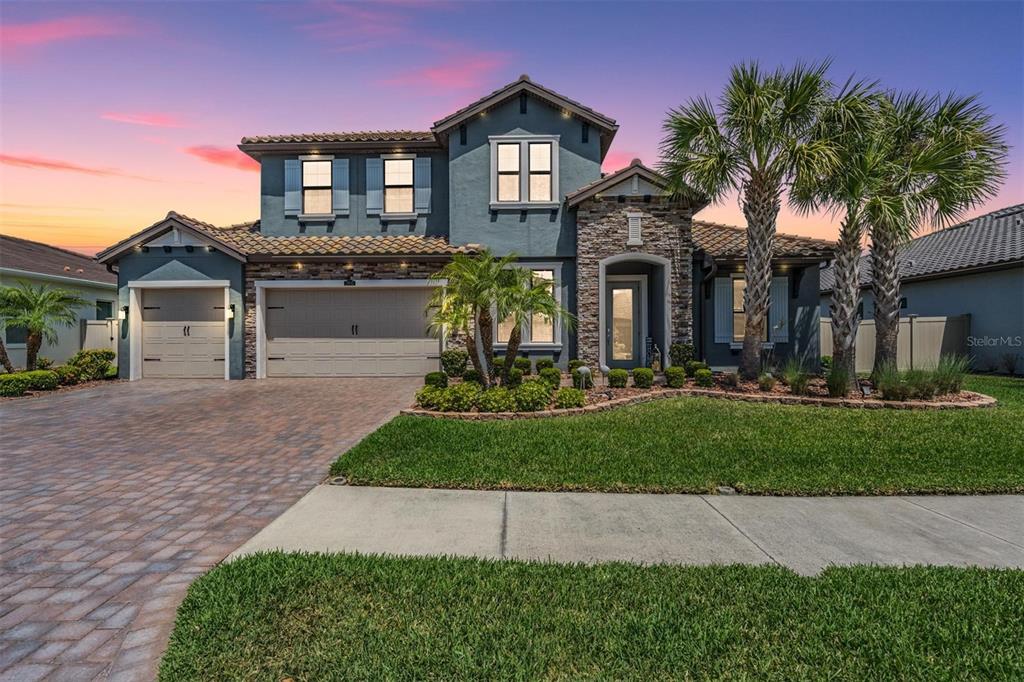 A two-story house with a stone facade, blue stucco, and a paved driveway at dusk — 29043 PICANA LANE, WESLEY CHAPEL, FL