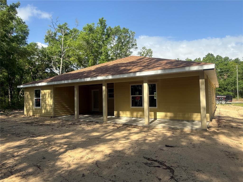 A yellow single-story house with a covered porch sits on a sandy, wooded lot — 551 NE STATE ROAD 121, WILLISTON, FL