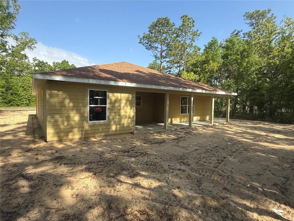 A newly constructed yellow house with a covered porch sits on a sandy lot — 551 NE STATE ROAD 121, WILLISTON, FL